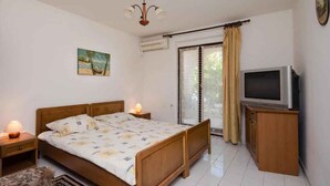 Un dormitorio con cama, lámparas de noche, un televisor sobre un mueble de madera y un cuadro en la pared.