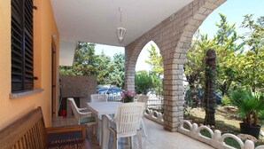 Un patio exterior con una mesa y sillas, un banco de madera y un arco de piedra.