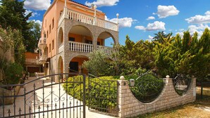 A multi-story building with a balcony, a gated entrance, and surrounding greenery. - Holiday apartment with air conditioning (Banjole)