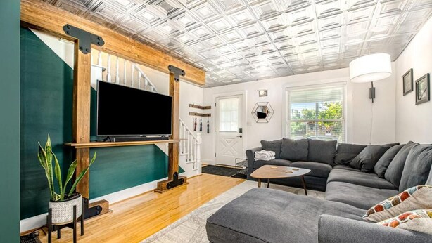 A modern living room with a large flat-screen TV, a grey sectional sofa, a coffee table, and a potted plant. - Downtown Three Oaks Home, Sleeps 6, Fire Pit, Walk to Shops (Three Oaks)