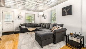 A modern living room with a sectional sofa, a small coffee table, and a side table with a router. - Downtown Three Oaks Home, Sleeps 6, Fire Pit, Walk to Shops (Three Oaks)