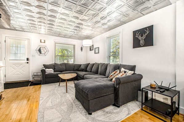 A modern living room with a sectional sofa, a small coffee table, and a side table with a router. - Downtown Three Oaks Home, Sleeps 6, Fire Pit, Walk to Shops (Three Oaks)