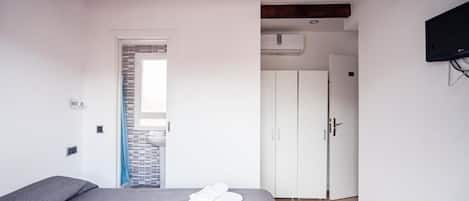 Une chambre à coucher avec un lit, une poutre en bois au plafond, une armoire blanche et un téléviseur fixé au mur.