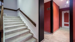Un escalier avec des rampes en bois menant à un palier doté d’un mur rouge et d’une enseigne.