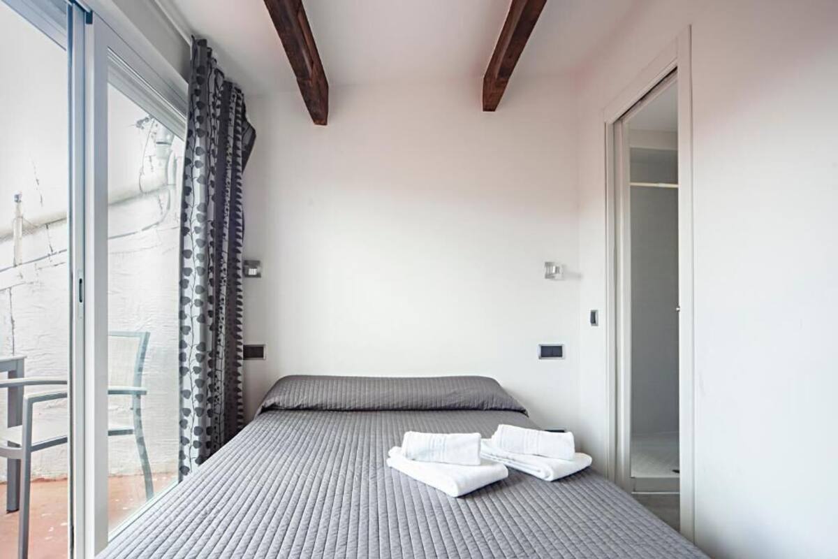 Un dormitorio con cama, una ventana con cortinas y una puerta que da a otra habitación.