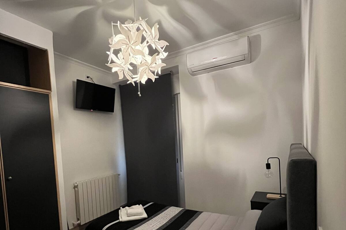 Un dormitorio moderno con cama, lámpara de techo, televisor en la pared y equipo de aire acondicionado.