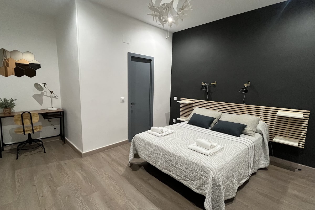Un dormitorio moderno con cama, mesitas de noche, un escritorio y una silla.