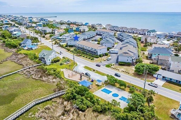 Vue aérienne d’une zone résidentielle côtière, avec des maisons, une plage et une jetée.