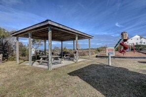 Un pavillon rustique en bois, doté de tables de pique-nique, entouré d’une aire de jeux avec un toboggan et une structure d’escalade.