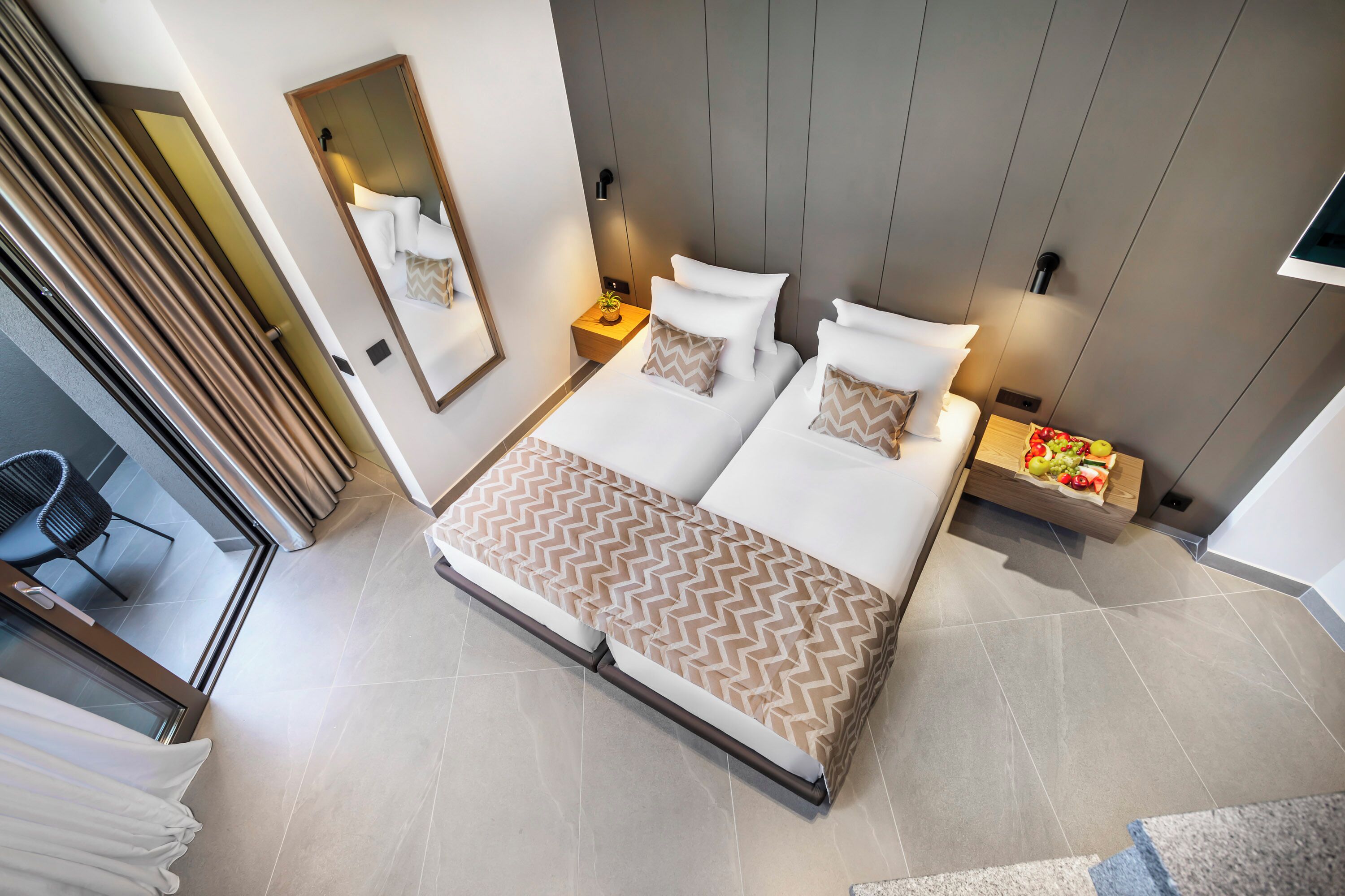 Una habitación de hotel moderna con una cama grande, mesitas de noche, un espejo y vistas al exterior.