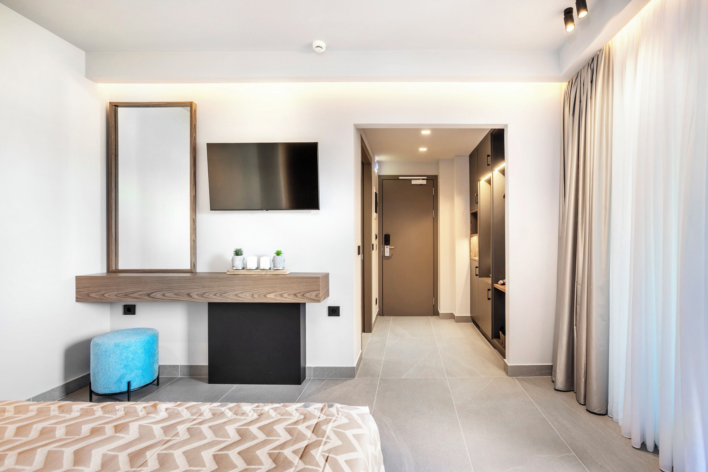 A modern hotel room with a large bed, a bedside table, a mirror, a flat-screen TV, and a bathroom visible through an open door.