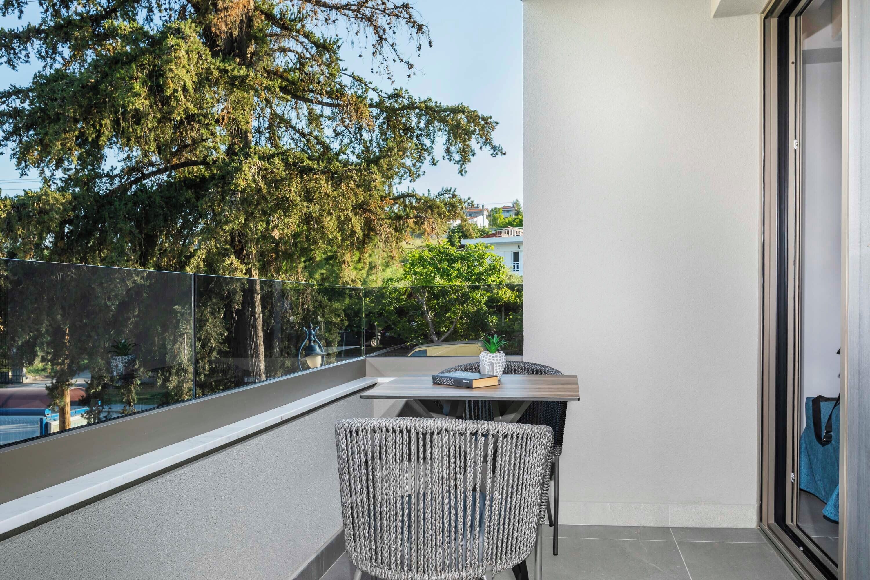 A balcony with a table and chair, a potted plant, and a view of trees and buildings.