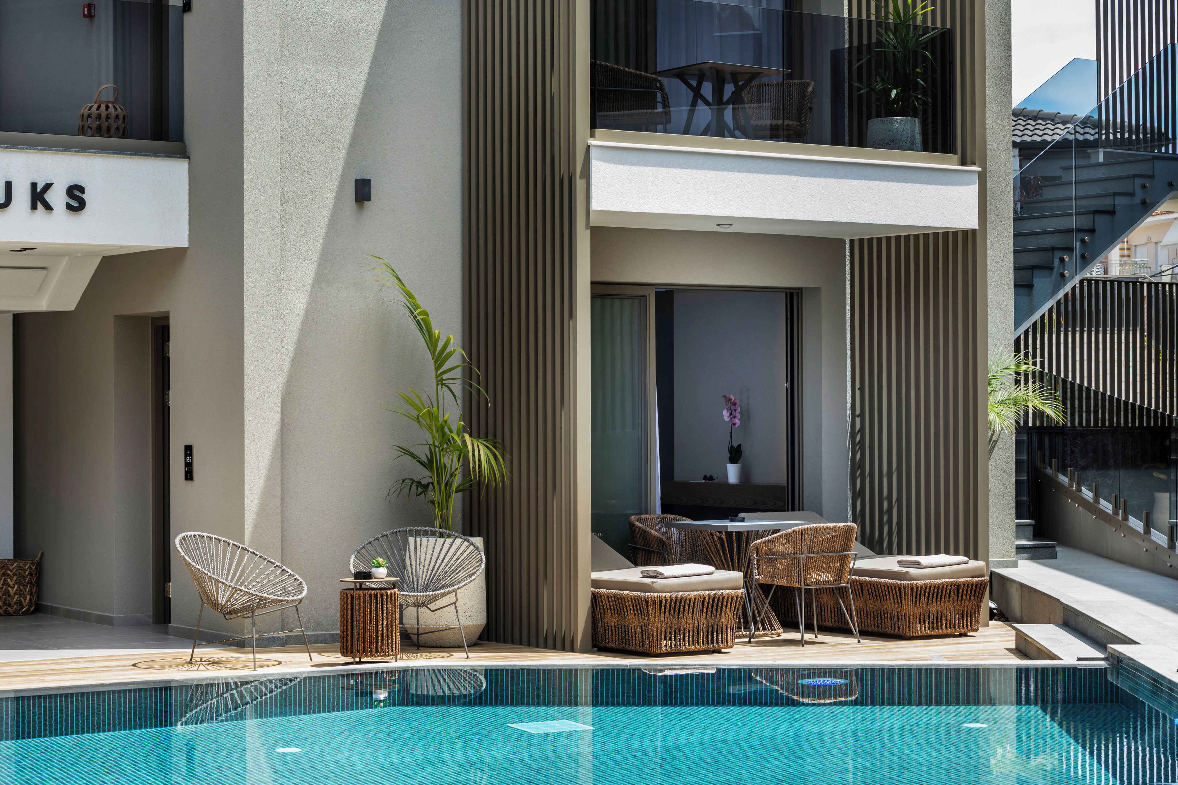 Un hôtel moderne doté d’une piscine et d’un espace aménagé avec des meubles en osier, offrant une vue sur l’intérieur du bâtiment.