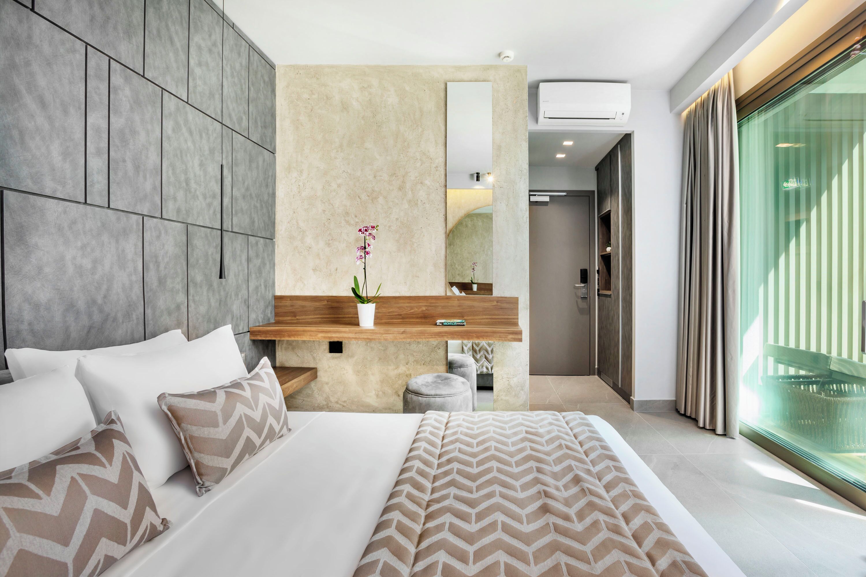 A modern bedroom with a large bed, a wooden bedside table, a mirror, and a view of the outside through a large window.