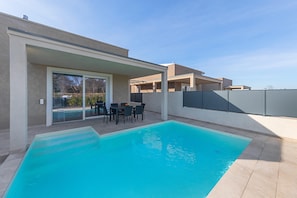 Een modern huis met een zwembad, terrasmeubilair en een overdekt buitengebied.