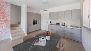 Une cuisine moderne avec des meubles gris, un four à micro-ondes et un évier. On y trouve une table à manger avec un magazine et un vase de fleurs.