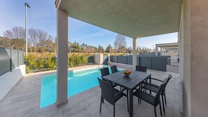 Un patio couvert avec une piscine, du mobilier d’extérieur et une vue sur les environs.