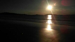 Een strandscène bij zonsondergang, met de zon die in het water schittert.