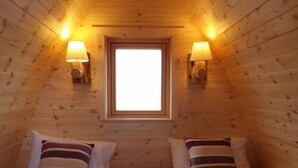 Een knus kamer in een chalet met twee bedden, elk met gestreepte kussens, een raam aan het einde en wandlampen.