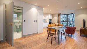 A modern living room with a dining area, a kitchen in the background, and a large window providing natural light. - Contemporary North London Flat (London)