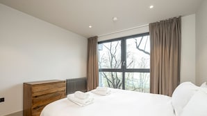 A modern bedroom with a large bed, a wooden dresser, and a window with curtains. - Contemporary North London Flat (London)