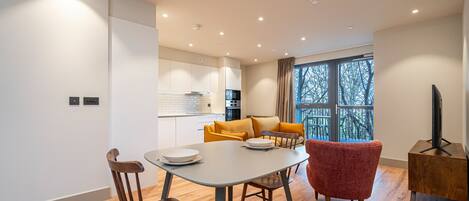 A modern living room with a dining table, two chairs, a sofa, and a TV stand.
