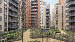 Un moderno complejo de apartamentos con varios pisos, balcones y un patio ajardinado con senderos y vegetación.