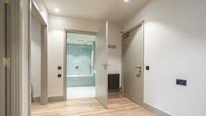 Un pasillo con piso de madera, una puerta que da a un baño con ducha y un radiador en la pared.