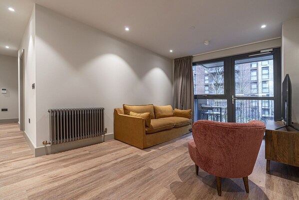 A modern living room with a sofa, armchair, and a large window with a city view.