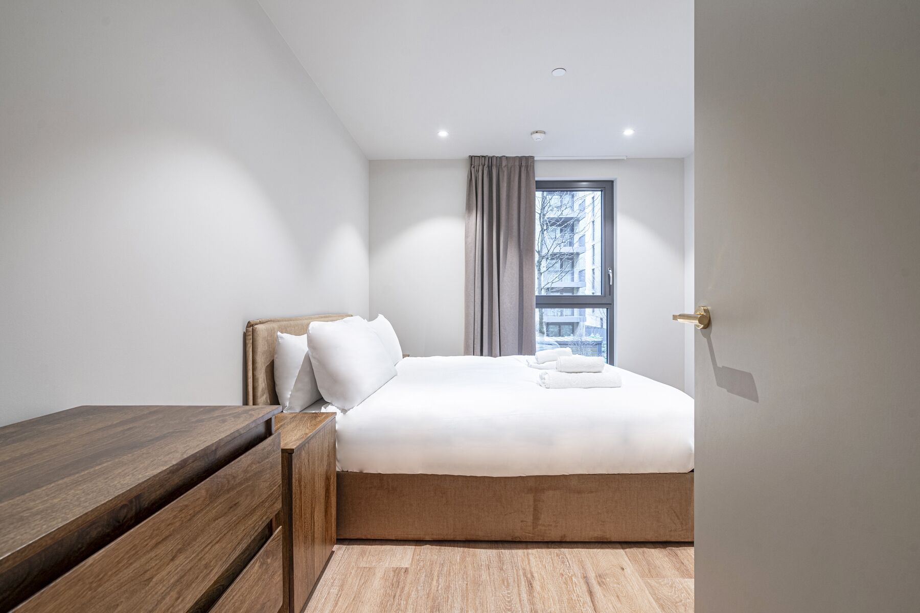 Ein schlichter Schlafzimmer mit einem Holzbett, einem Nachttisch und einem Fenster mit Vorhängen.