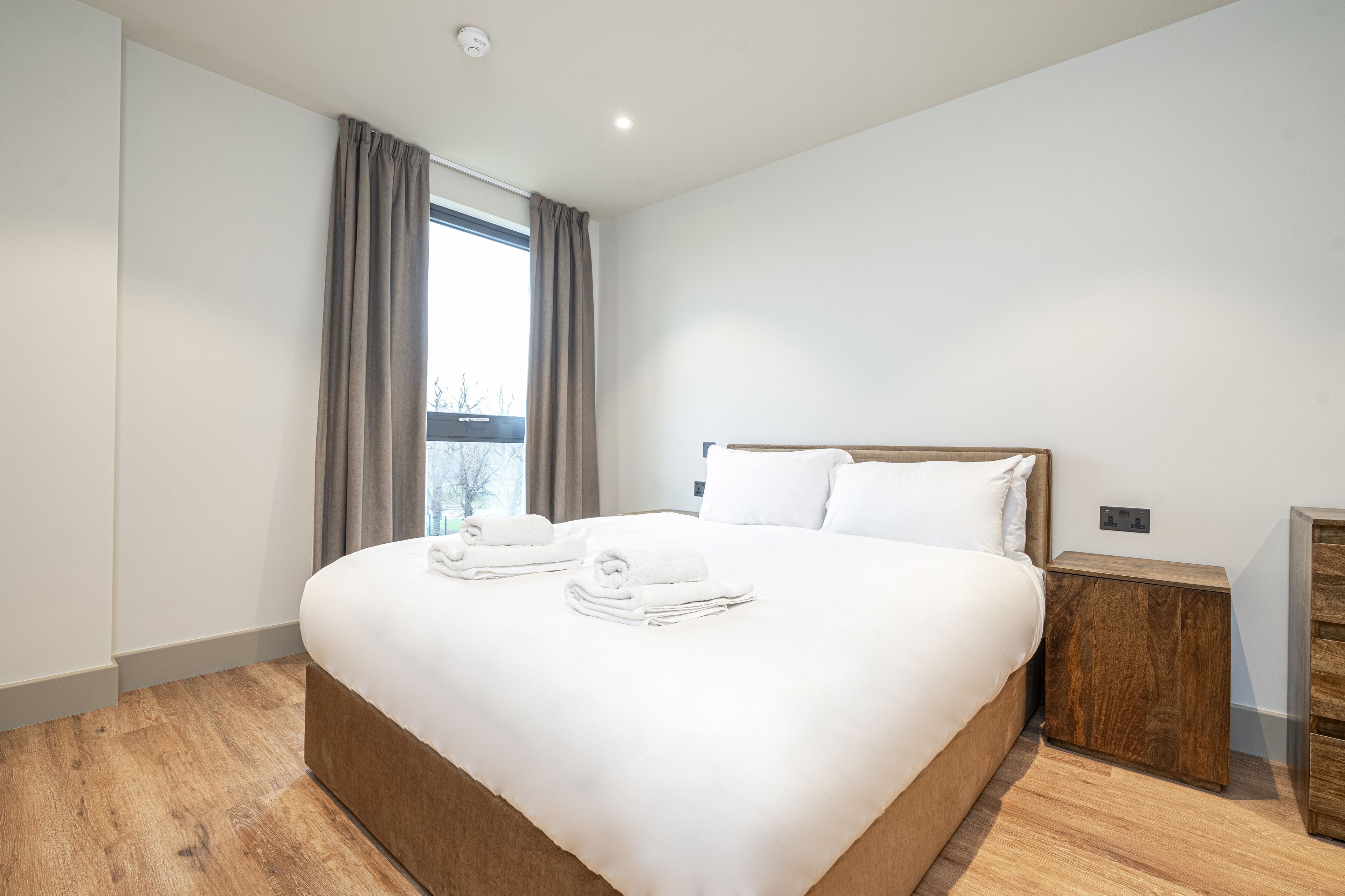 A modern hotel room with a large bed, wooden nightstands, and a view of the outdoors.