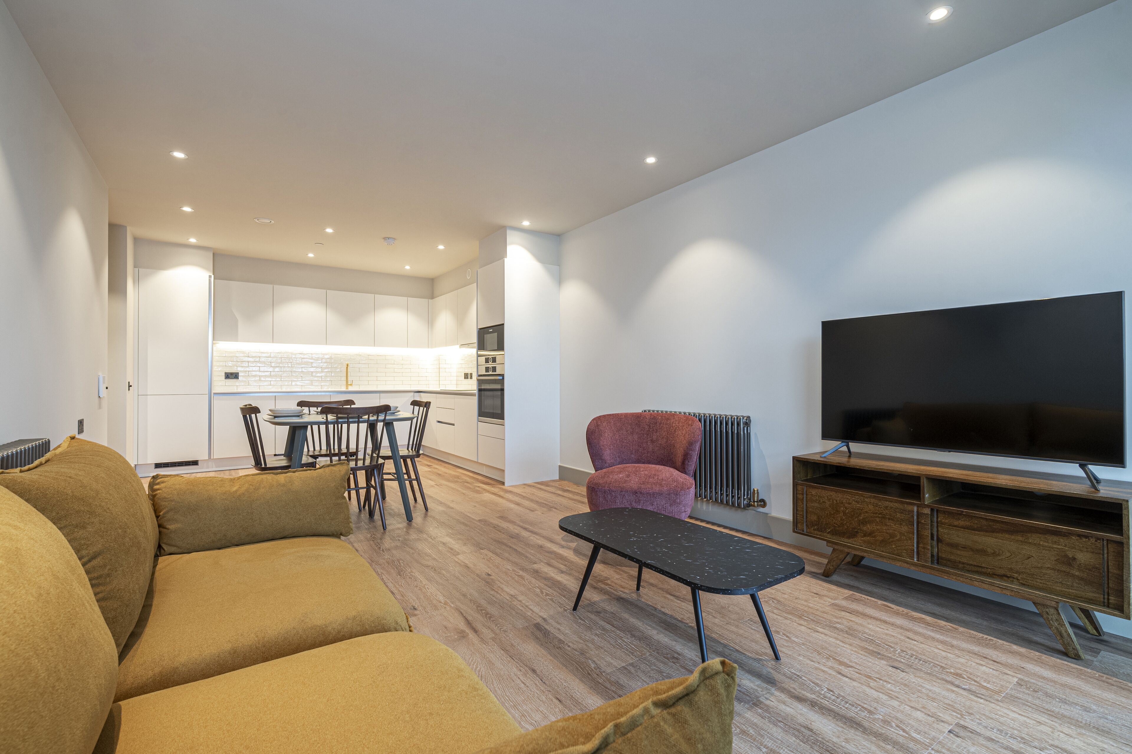 Ein modernes Wohnzimmer mit einer Couch, einem Couchtisch, einem Fernseher und einem Essbereich mit Stühlen und einem Tisch.