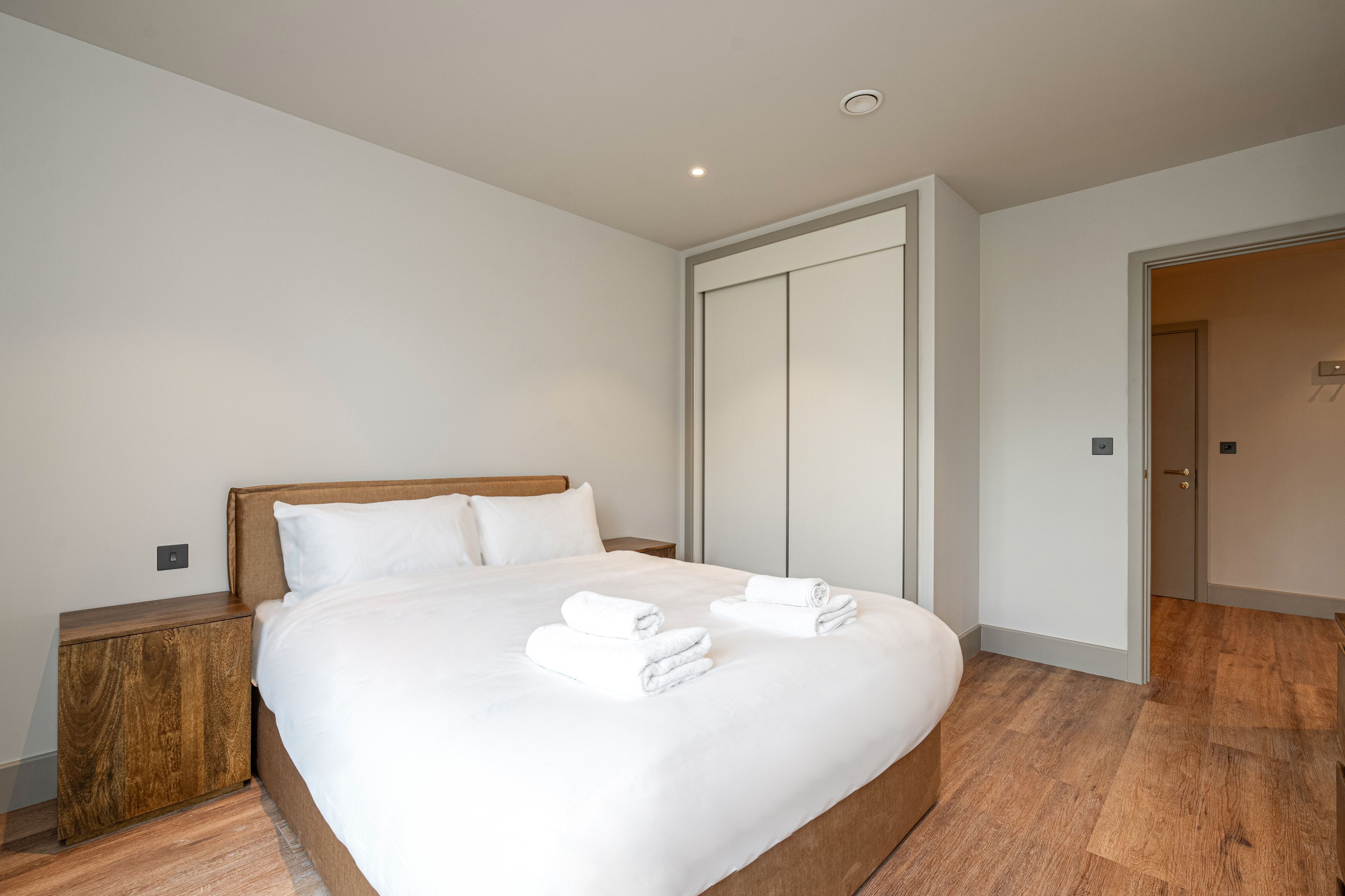 A modern hotel room with a large bed, wooden nightstand, and a wardrobe.