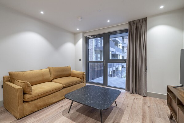 A modern living room with a sofa, a coffee table, and a large sliding glass door leading to a balcony.