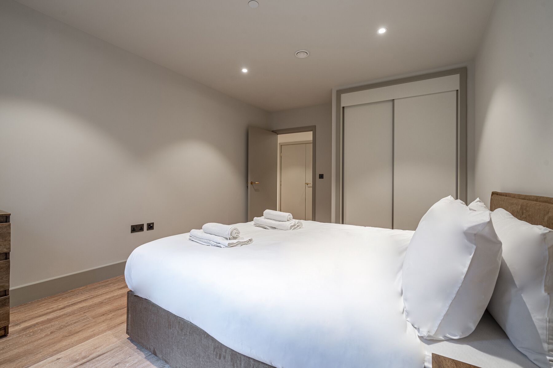 Un dormitorio moderno con una cama grande, una mesita de noche de madera y una puerta que da a otra habitación.
