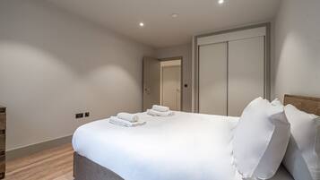 Un dormitorio moderno con una cama grande, una mesita de noche de madera y una puerta que da a otra habitación.