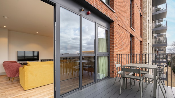 A modern apartment with a balcony, a yellow sofa, a dining table, and a TV. - Spacious Flat in North London (London)