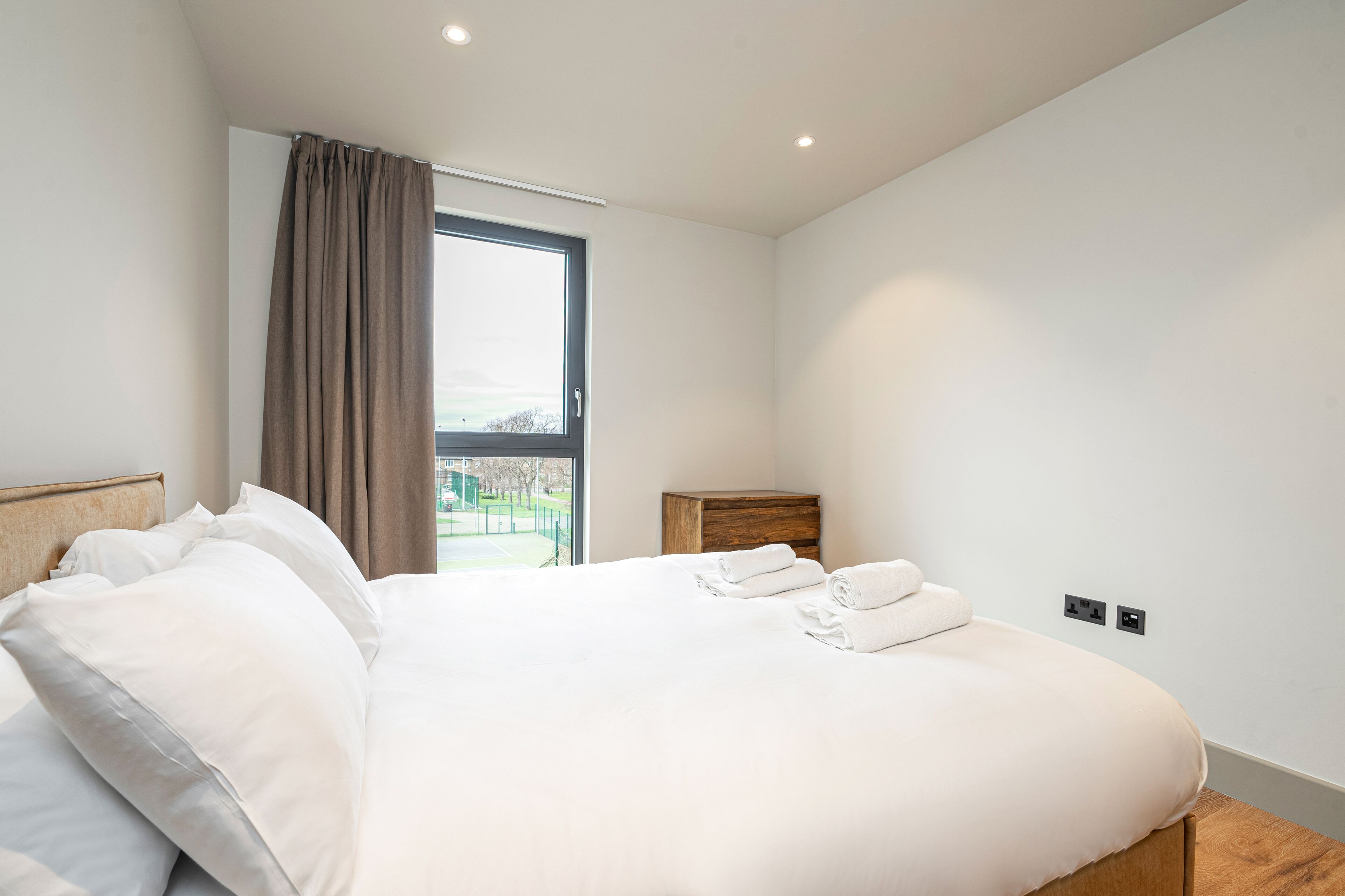 A modern hotel room with a large bed, a wooden nightstand, and a window with curtains.