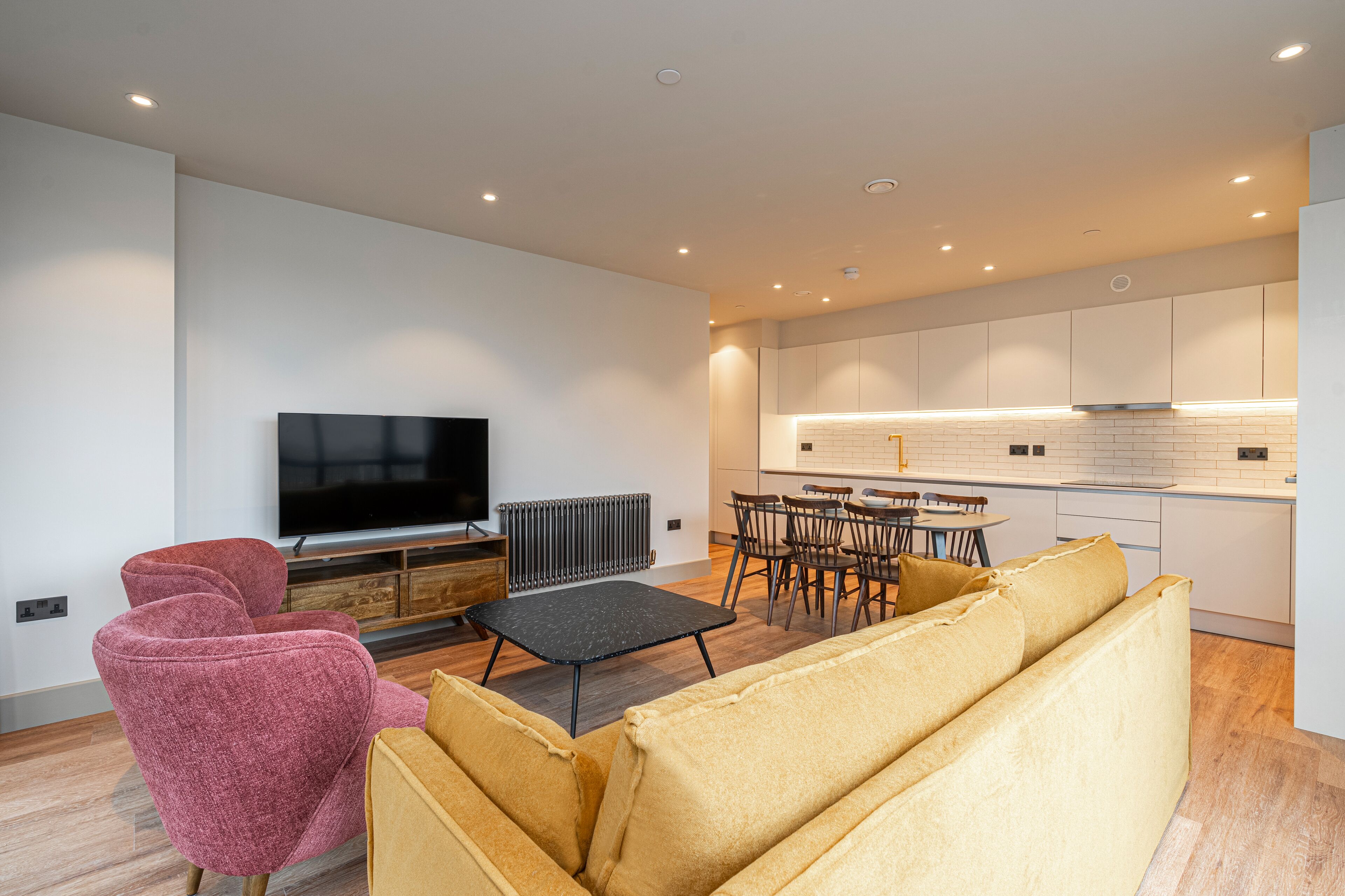 Un salon moderne comprenant un canapé, des fauteuils, un téléviseur et un coin repas avec une table et des chaises.