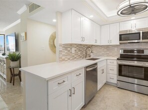 A modern kitchen with white cabinetry, a tiled backsplash, stainless steel appliances, and a central island.