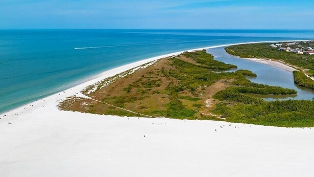An aerial view of a beach with a clear sky, a sandy shore, and a narrow strip of vegetation separating the beach from the water. - Beachfront 2BR/2BA condo with pool, WiFi, and Marco Island views. (Marco Island)