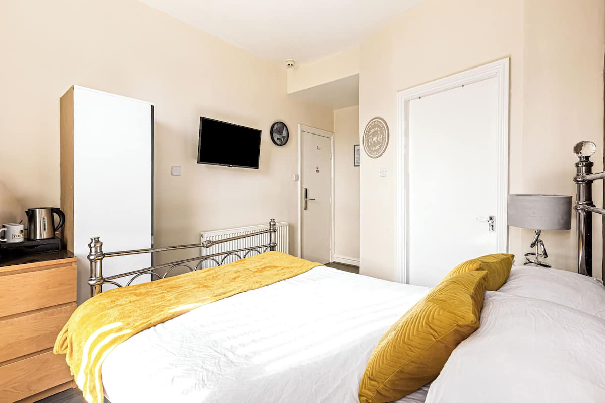 Une chambre d’hôtel avec un lit, un téléviseur fixé au mur, une porte et une table de chevet avec une lampe.
