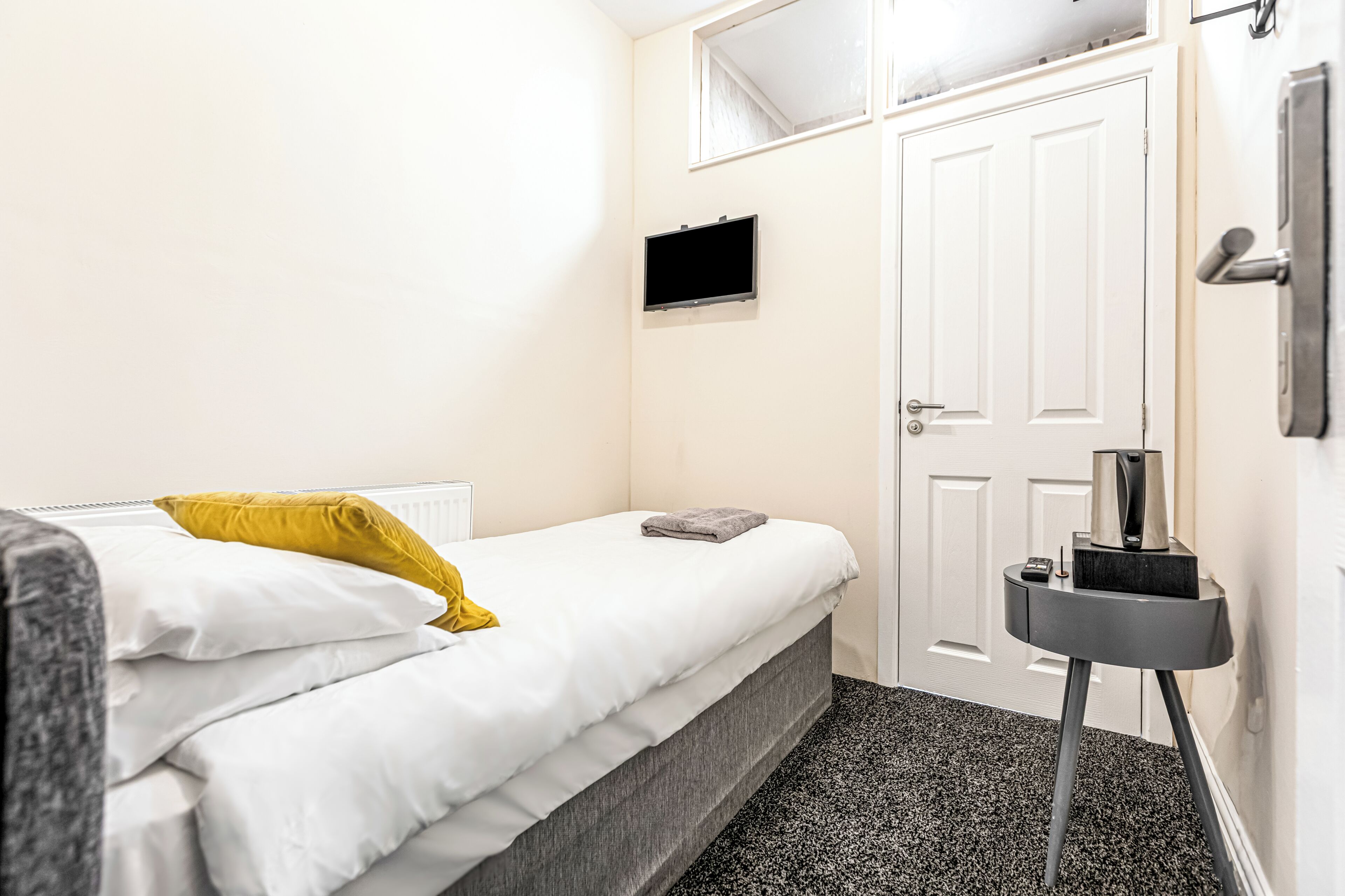 A bedroom with a bed, a small bedside table, a TV, and a door.