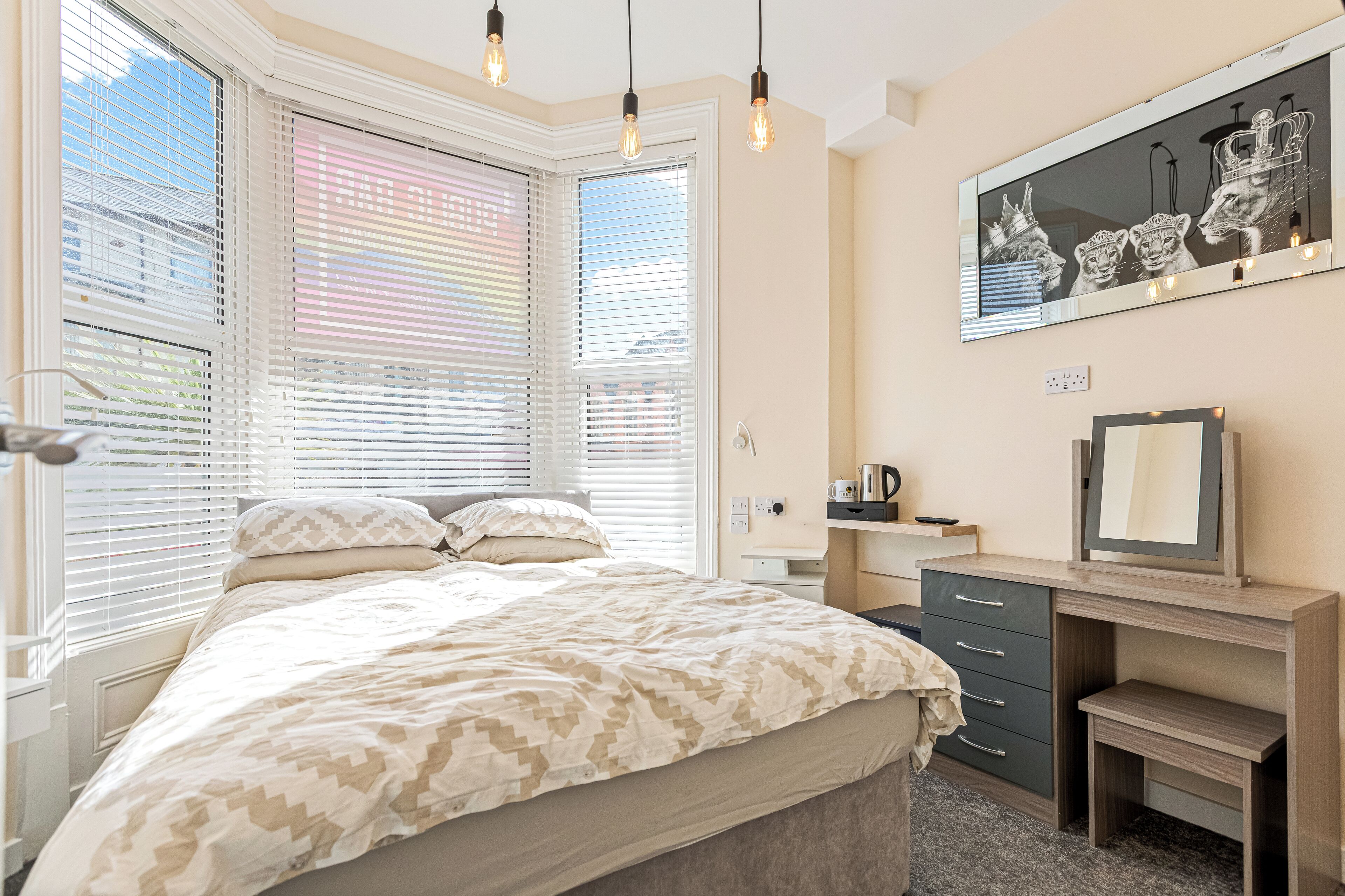 A bedroom with a bed, a desk, a chair, a dresser, a mirror, and a window with blinds.