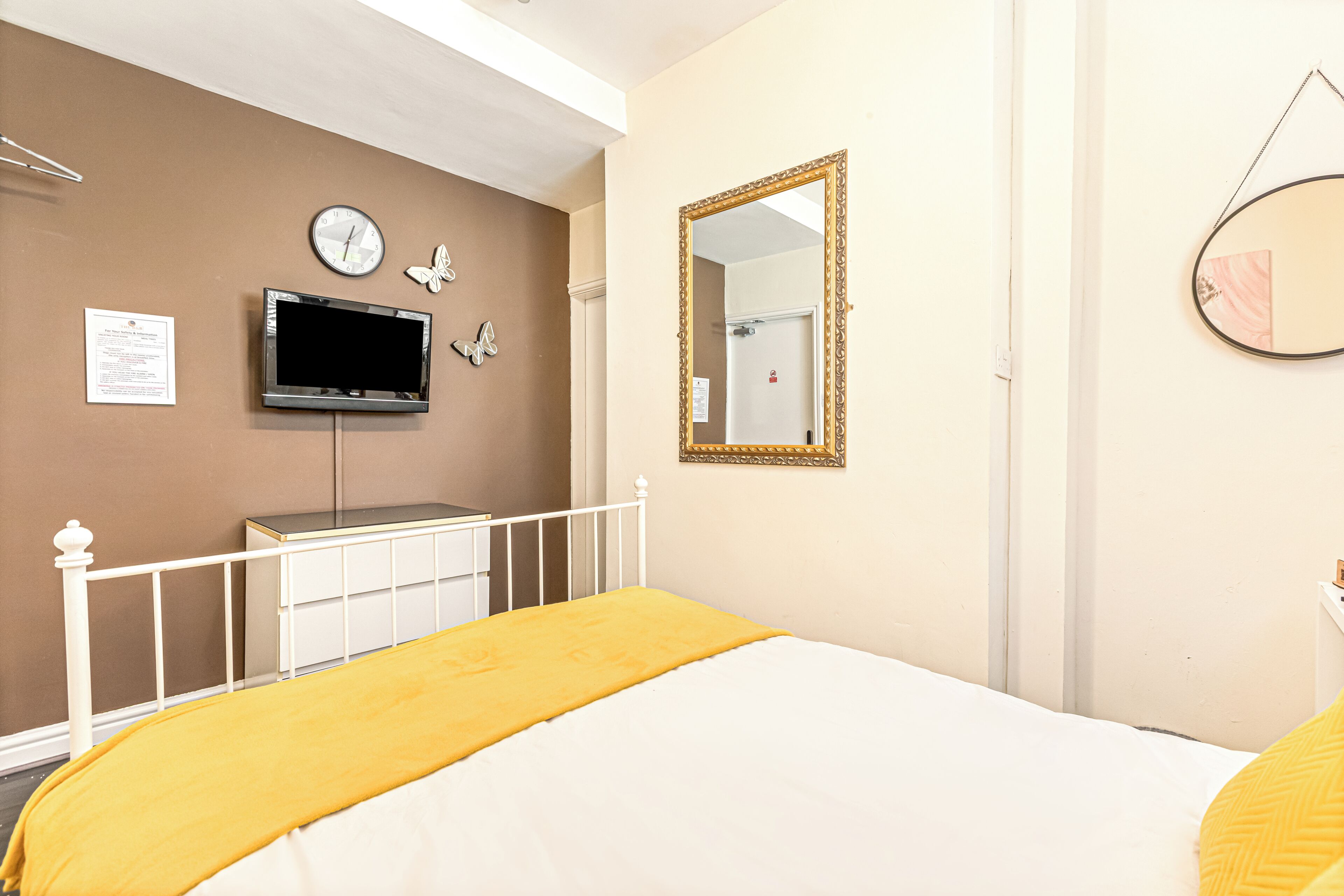 Un dormitorio con cama, televisión, espejo y un reloj en la pared.