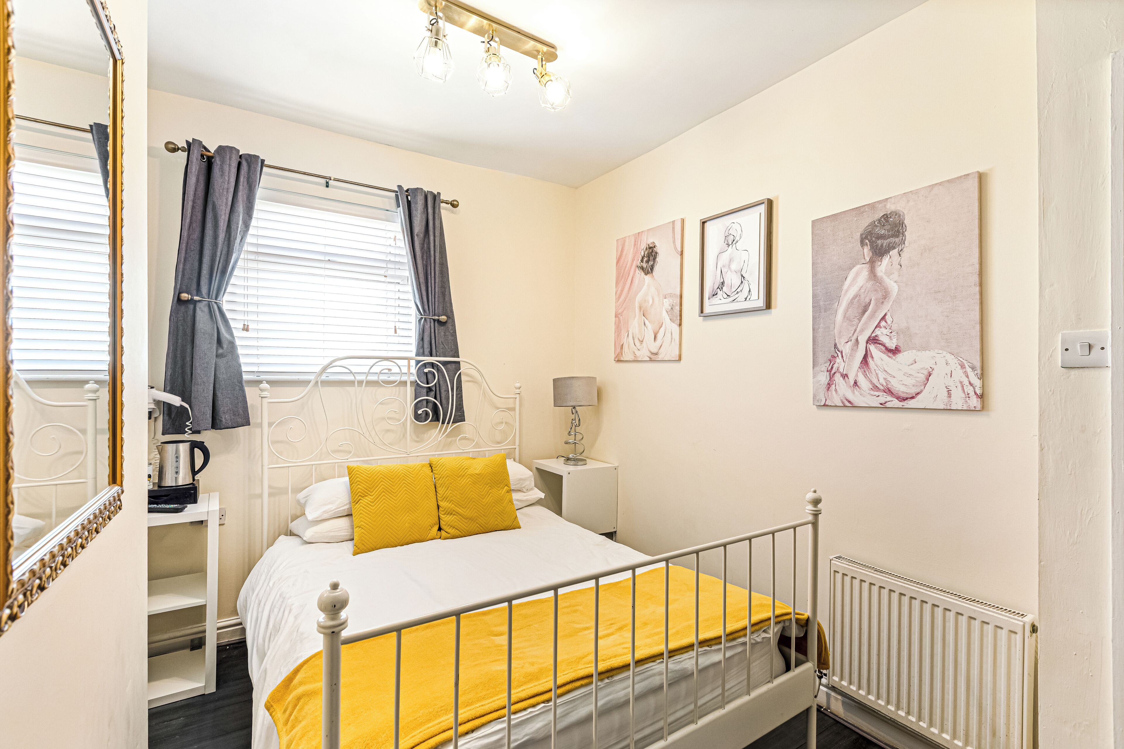 A bedroom with a bed, a nightstand, a lamp, a radiator, and artwork on the wall.