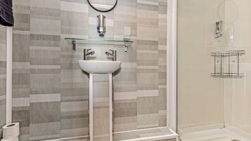 A modern bathroom with a glass shelf, a white sink, and a shower area.