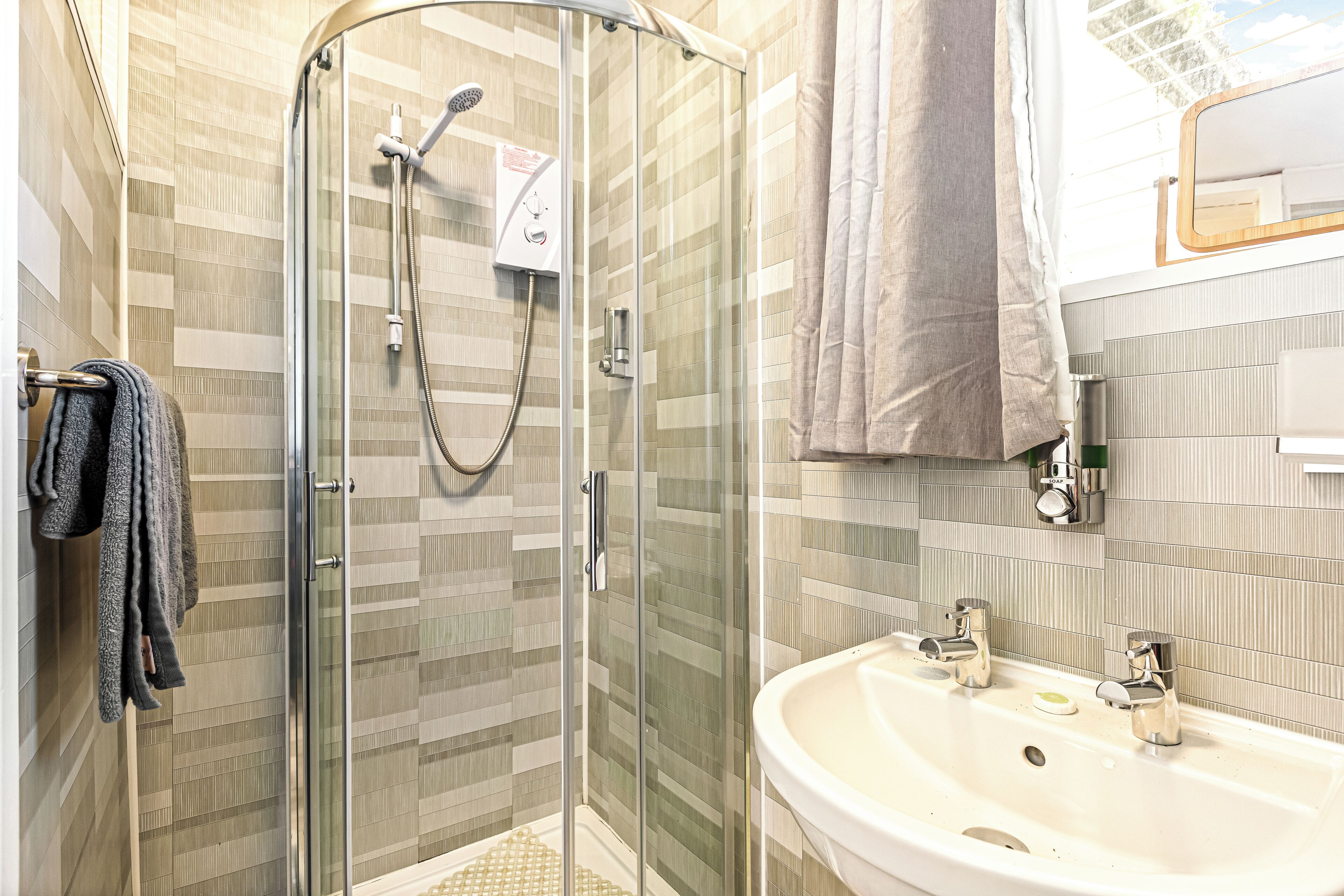 Een badkamer met een douche met glazen wand, een wastafel met twee kraan en een handdoekrek met handdoeken.
