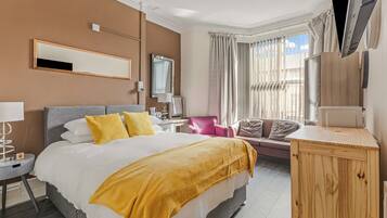 Een hotelkamer met een groot bed, een bureau, een stoel, een televisie en een raam met gordijnen.