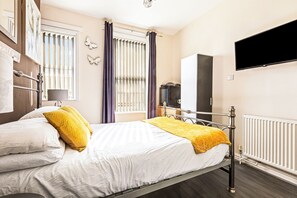 A bedroom with a bed, a television mounted on the wall, a radiator, and a window with curtains. - The B & B Blackpool (Blackpool)
